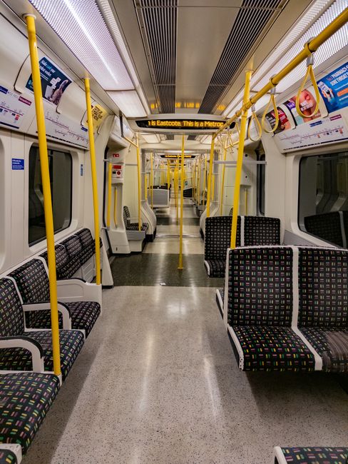 A close-up view of a section of the London Underground train platform, focusing on multiple train doors with reflective surfaces showcasing the yellow safety strips along the platform edge and the tra